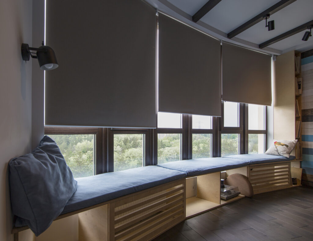 Dark roller blinds designed by Australian Plantation Shutters covering tall windows above a window seat.