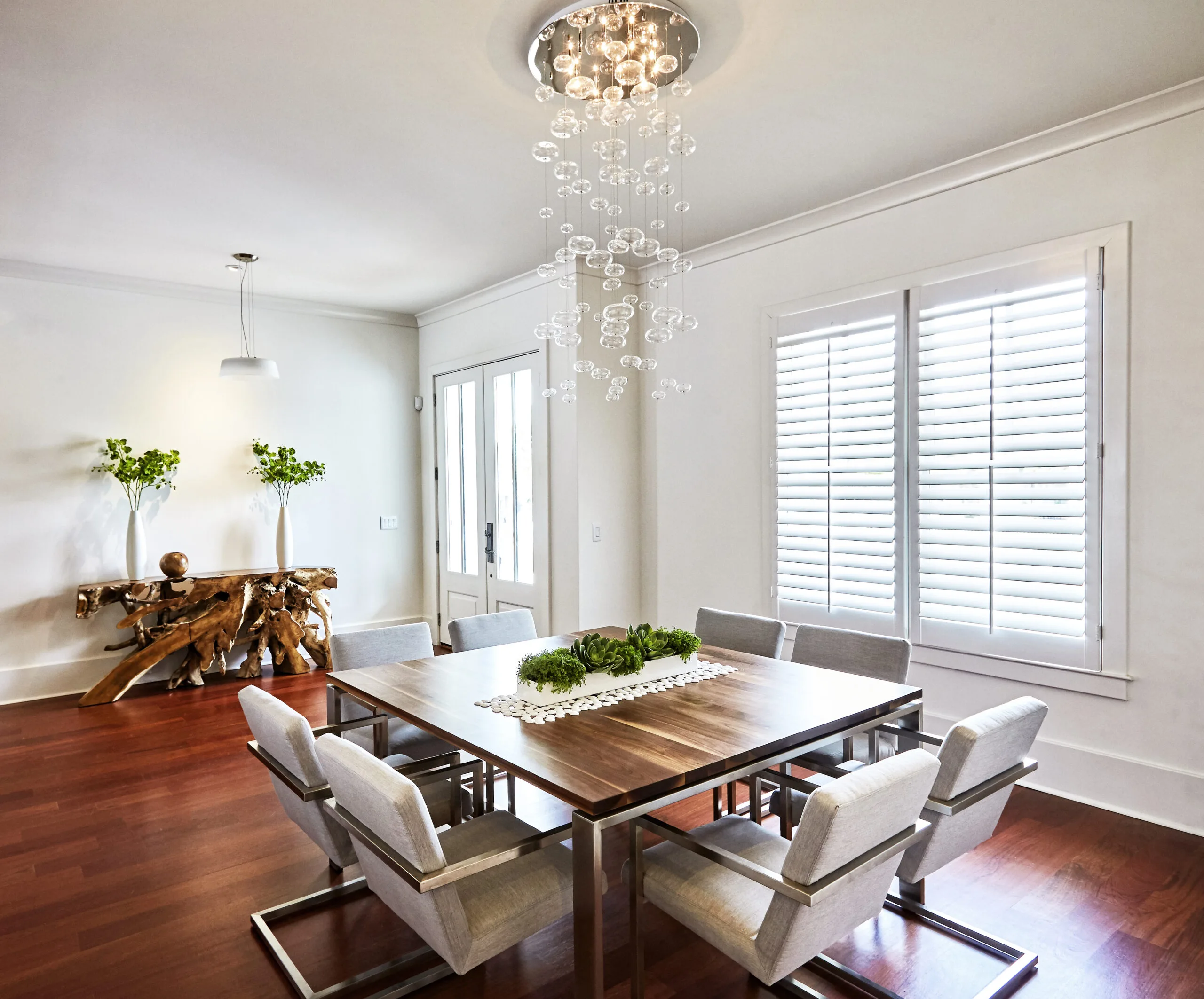 White plantation shutters designed by Australian Plantation Shutters installed beside a dining area with chandelier.