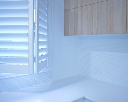 White plantation shutters designed by Australian Plantation Shutters installed beside wooden kitchen cabinets.
