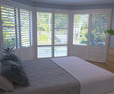White plantation shutters designed by Australian Plantation Shutters installed around corner windows in a bedroom.
